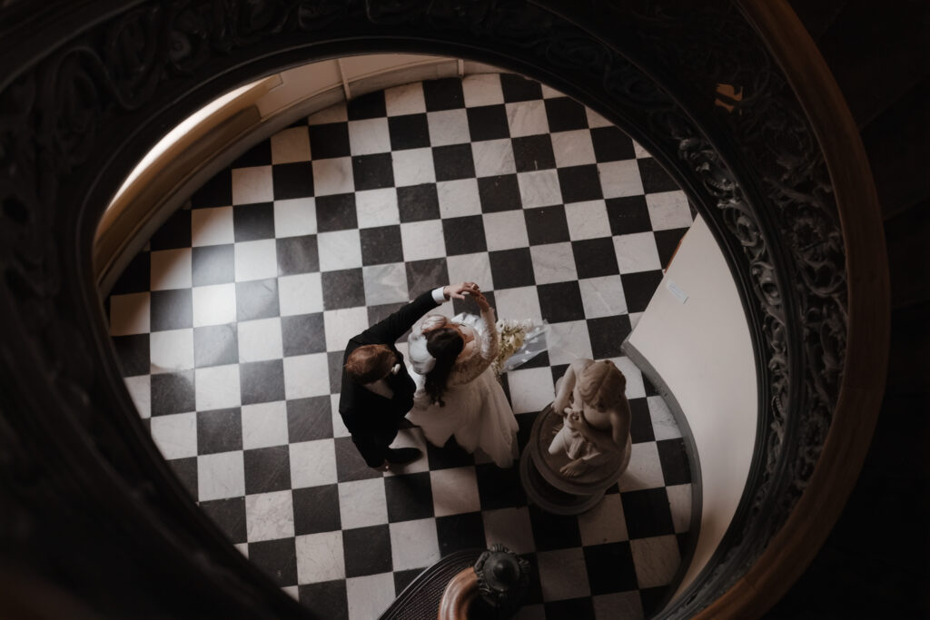 Baltimore wedding photographer captures bride and groom dancing under the George Peabody Library staircase on a black and white marble floor.