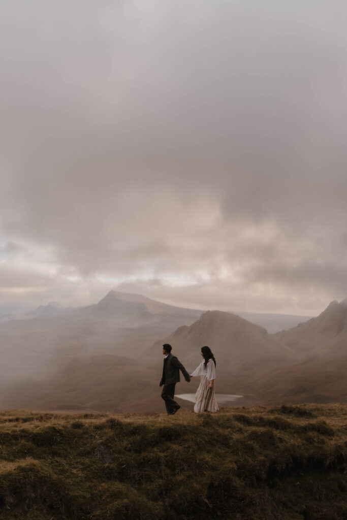 Couple walking hand in hand across the Quiraing during a cinematic Isle of Skye couples photoshoot in the Scottish Highlands.
