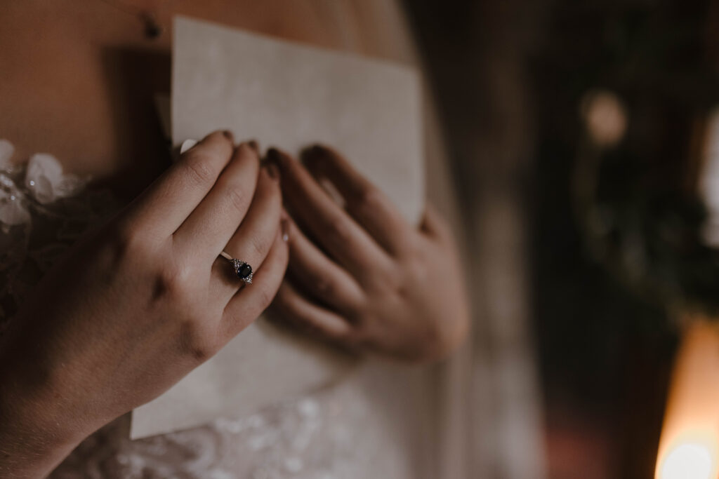 Close-up detail of Bethany’s sapphire engagement ring as she holds a handwritten letter during bridal prep at Kilmartin Castle.