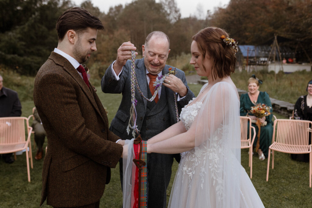 Handfasting ceremony at Kilmartin Castle, with Bethany’s father tying symbolic fabric strips around the couple’s hands during their autumn Scottish wedding.