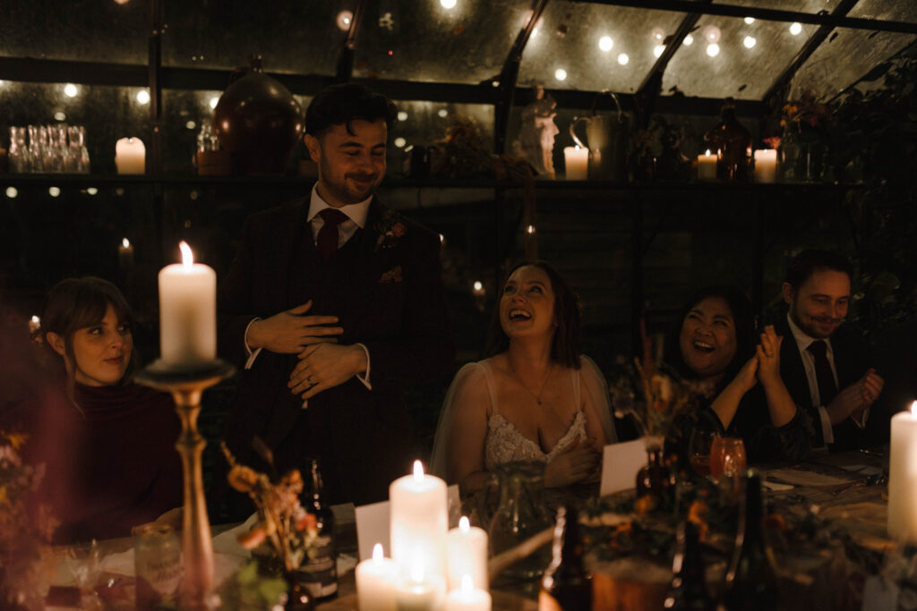 Adam giving his wedding speech in Kilmartin Castle’s candlelit greenhouse, surrounded by autumn florals, warm candlelight, and cheering guests during this intimate Scotland wedding.