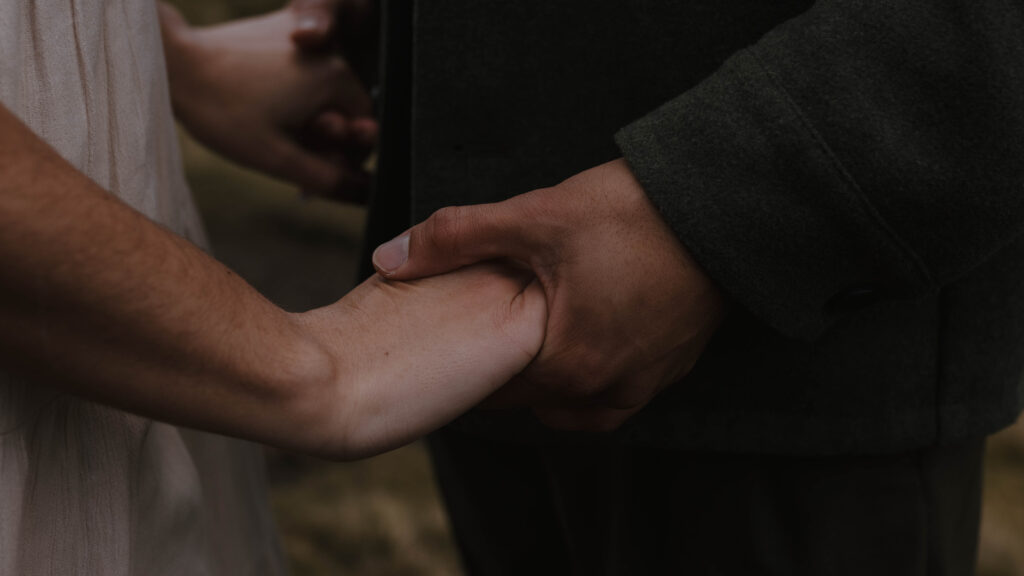 Close-up of a couple holding hands during an Isle of Skye couples session, photographed in a moody, fine art style by Scotland elopement photographer Aly Robinson.
