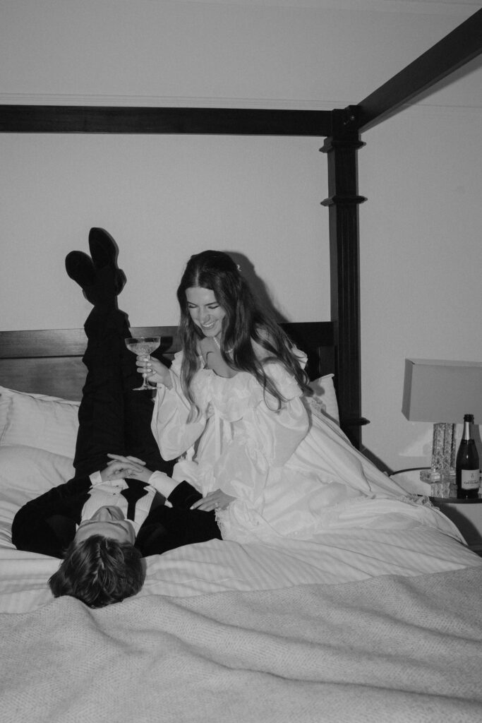 Playful wedding morning moment with a bride laughing on a hotel bed while the groom relaxes beside her, captured in a relaxed editorial style by Aly Robinson, Scotland wedding photographer.