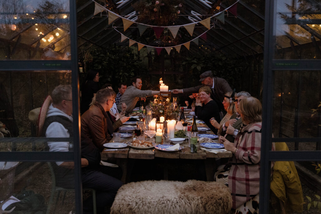 Intimate greenhouse wedding dinner with guests sharing food by candlelight, photographed in a warm documentary style by Scotland wedding photographer Aly Robinson.
