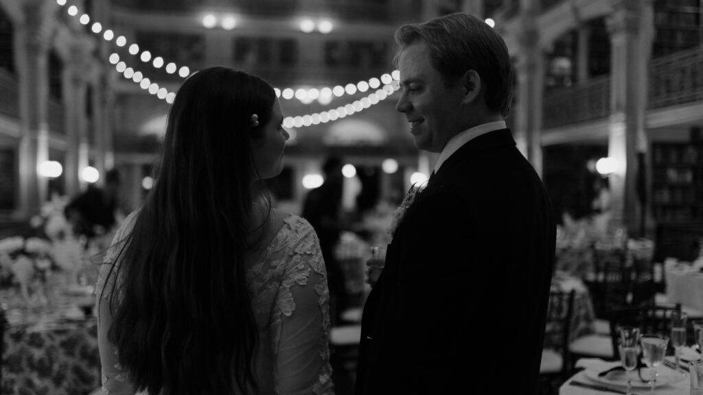 Cinematic black and white wedding portrait of a couple smiling at each other under string lights in an ornate reception hall, photographed by Scotland wedding photographer Aly Robinson