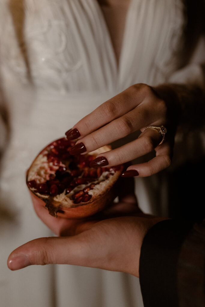 Close up of bride’s hands with engagement ring holding pomegranate fruit styled for dark romance wedding details at Prestonfield House Edinburgh