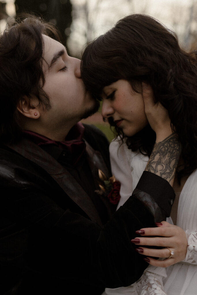 Groom kissing bride’s forehead during intimate outdoor portrait at Prestonfield House Edinburgh captured in cinematic luxury wedding photography style