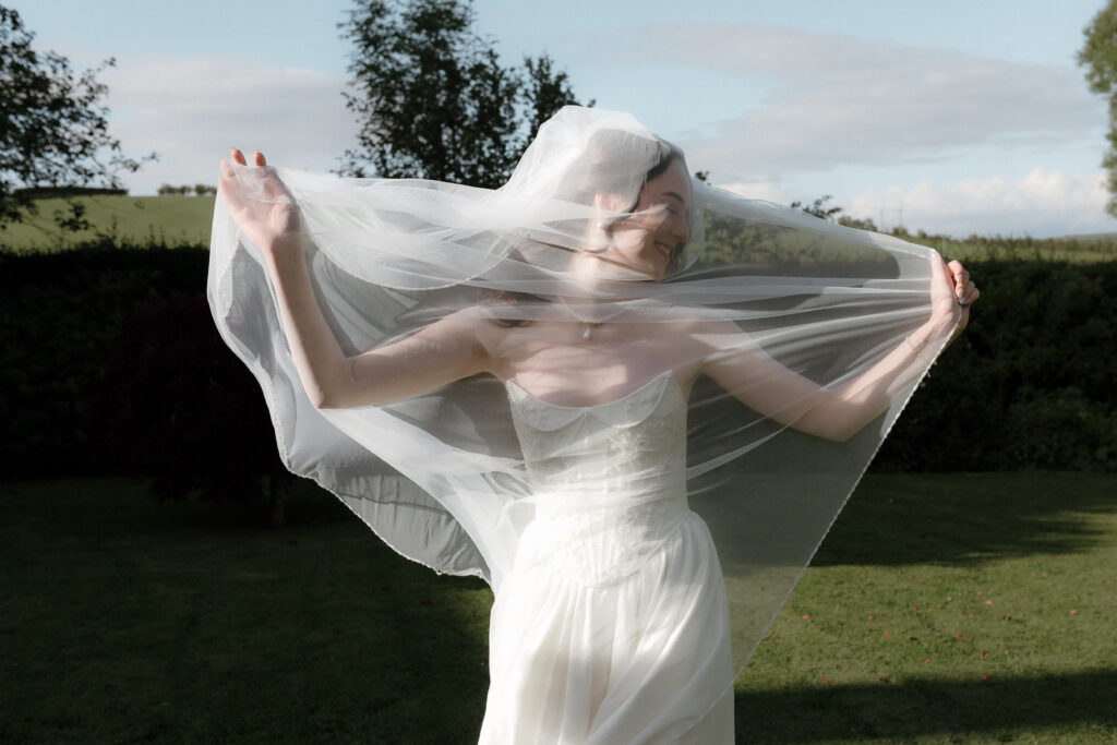 Bride playing with her veil in the summer sunshine during a luxury Scotland wedding at Dalduff Farm